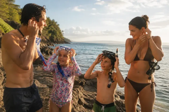 A family adjusting snorkel masks and SubMergence headsets at the water's edge