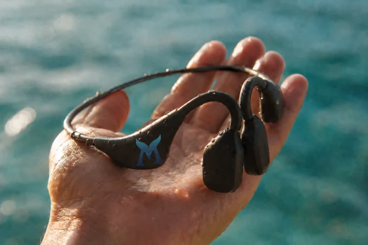 A waterproof SubMergence headset held over turquoise water
