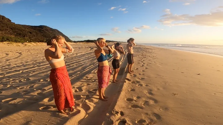 Four friends putting on SubMergence headsets along the shoreline as the sun sets over Kaua'i