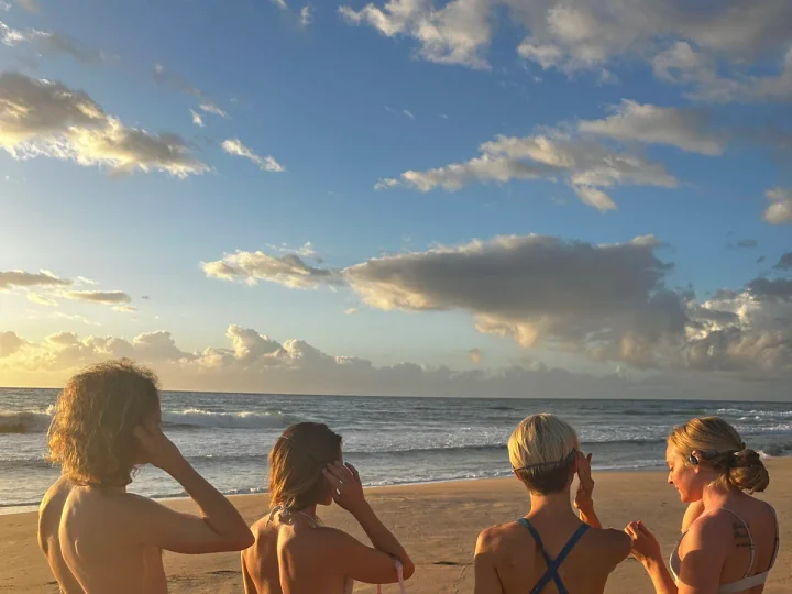 Four friends standing at the shoreline in SubMergence headsets, watching the sunset over the ocean on Kaua'i