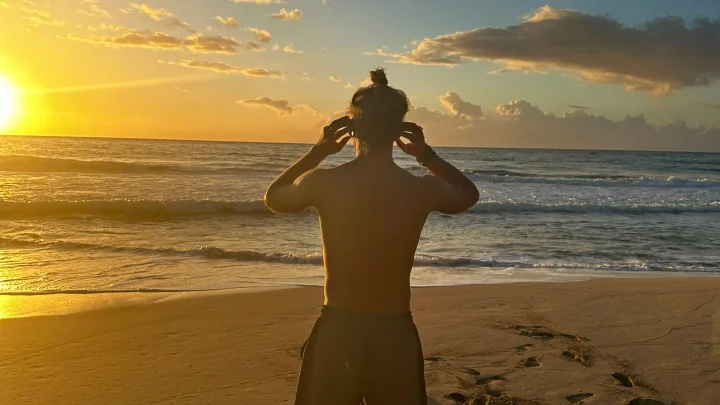 A swimmer fitting a SubMergence headset while facing a golden sunset over the ocean