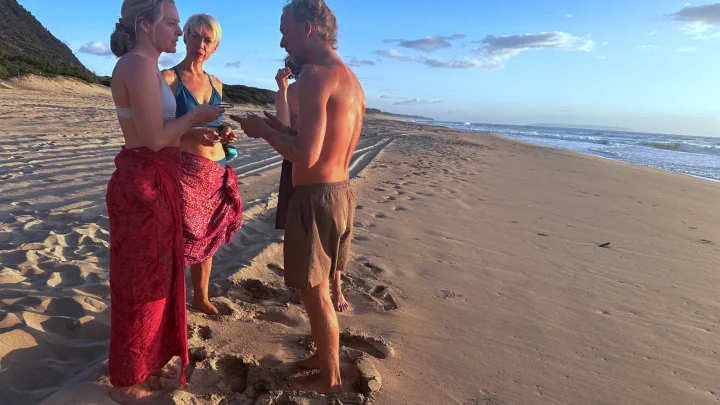 Alex helping two friends fit SubMergence bone-conduction headsets before an ocean swim at golden hour