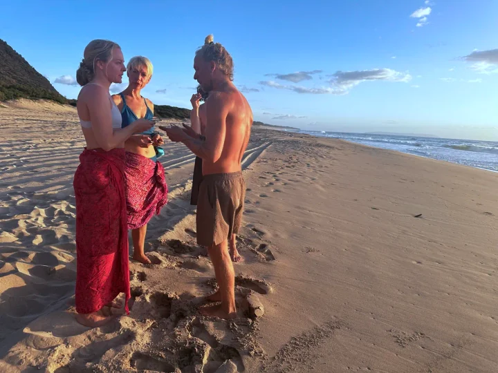 SubMergence founder Alex helping two friends fit bone-conduction headsets before an ocean swim at golden hour