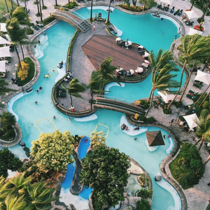 Aerial view of a tropical resort pool complex with palm trees, bridges, and guests in turquoise water