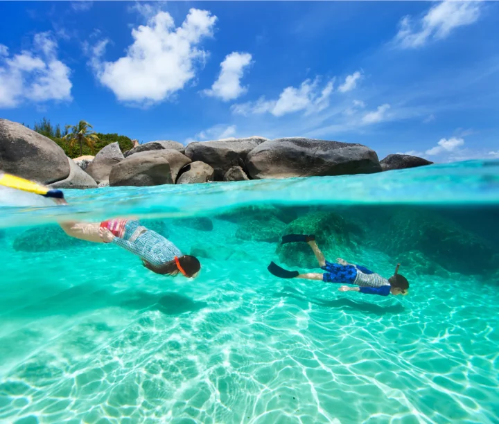 Split-level view of two snorkelers swimming near boulders in clear tropical water