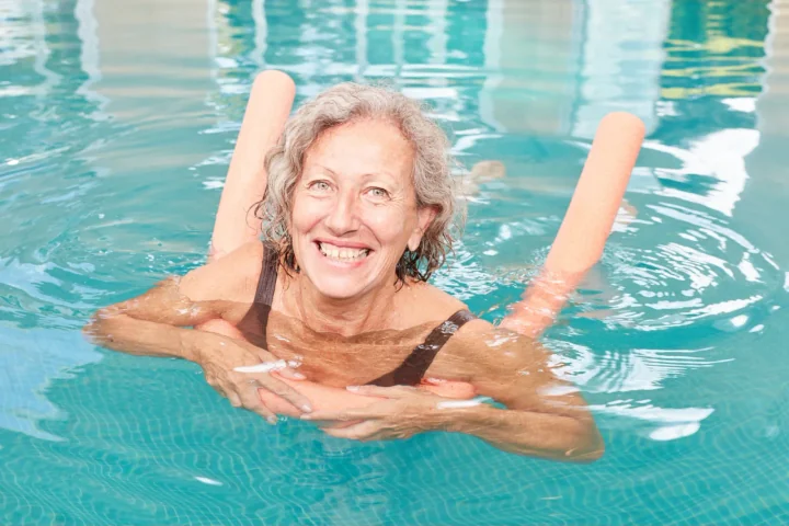 A smiling adult floating in a bright pool with orange pool noodles