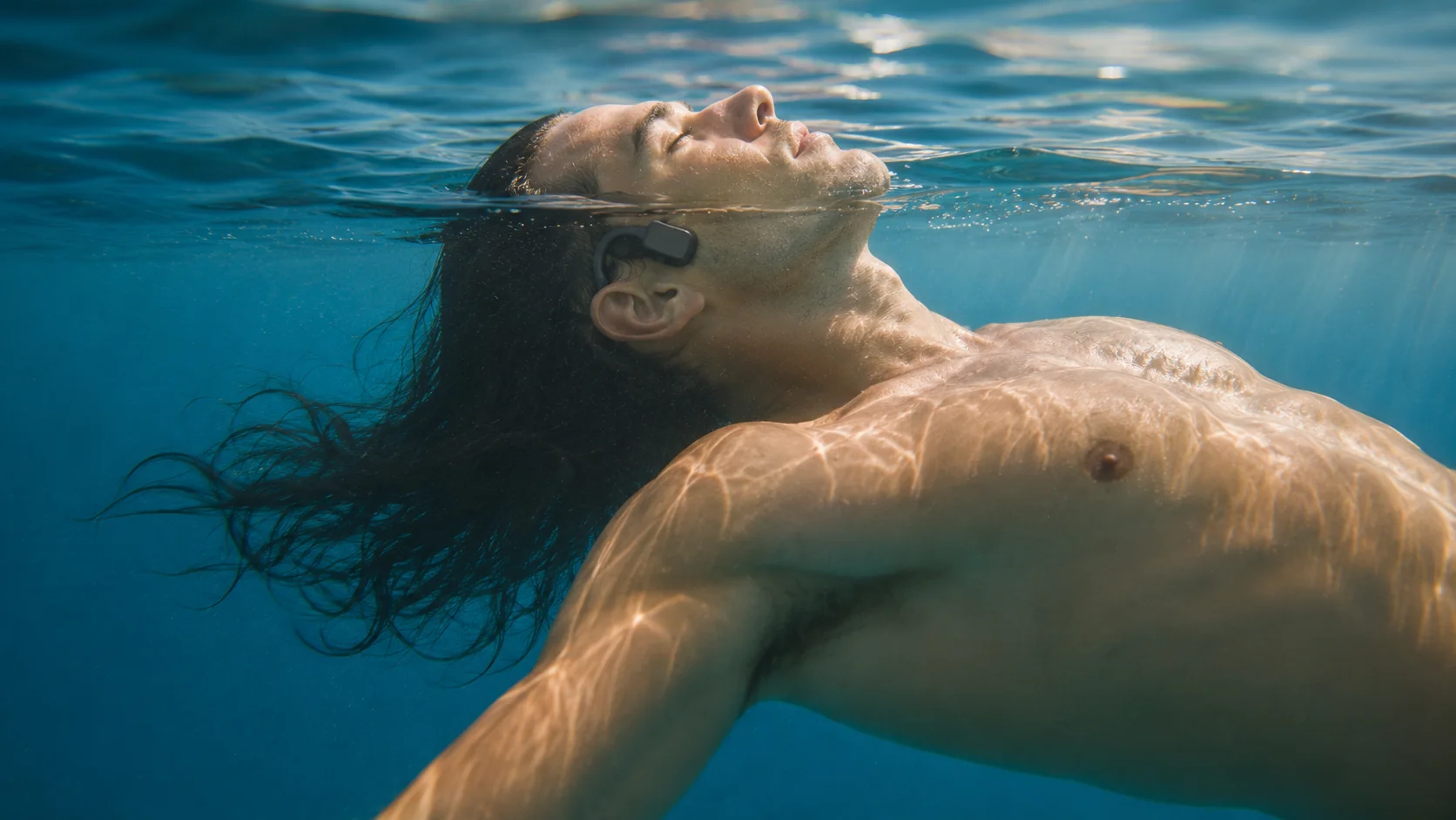 A swimmer floating serenely at the waterline while wearing a SubMergence headset