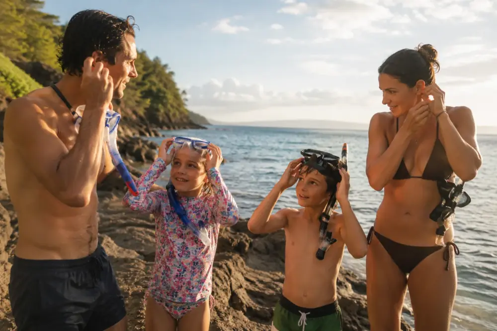 A family adjusting snorkel masks and SubMergence headsets at the water's edge