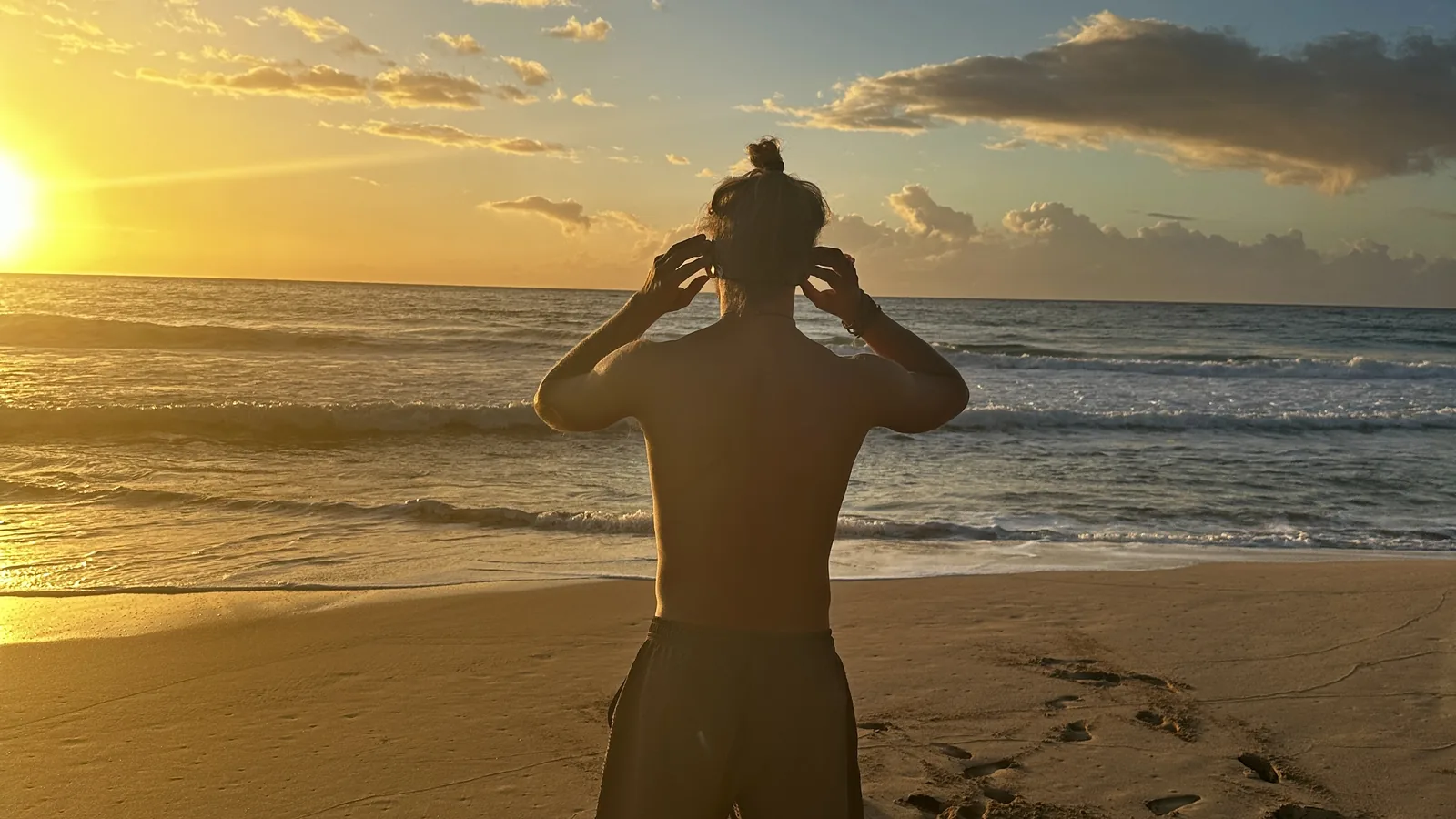 A swimmer fitting a SubMergence headset while facing a golden sunset over the ocean